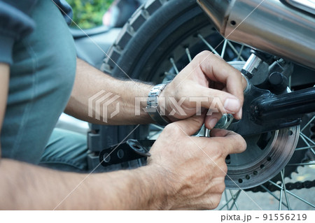 close up technician worker hand, fixed motocycle wheel at the outside of garage. close up technician worker hand, fixed motocycle wheel at the outside of garage. 91556219
