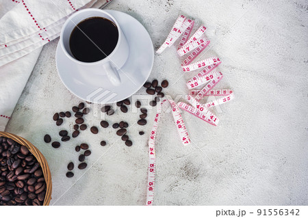 Cup of coffee and coffee beans background with measure tap on white desk. Cup of coffee and coffee beans background with measure tap on white desk. 91556342
