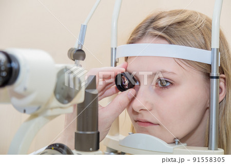 A male ophthalmologist checks the eyesight of a young girl using a modern device with a light beam A male ophthalmologist checks the eyesight of a young girl using a modern device with a light beam 91558305
