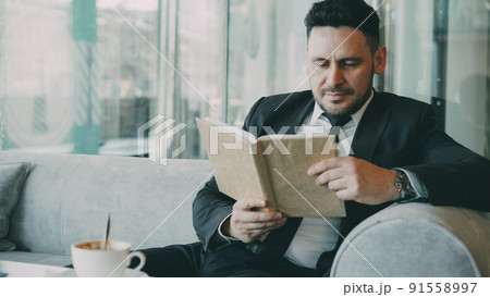 Successful Smart Caucasian businessman in formal clothes reading text book with and drinking coffee in classy cafe at lunch break Successful Smart Caucasian businessman in formal clothes reading text book with and drinking coffee in classy cafe at lunch break 91558997
