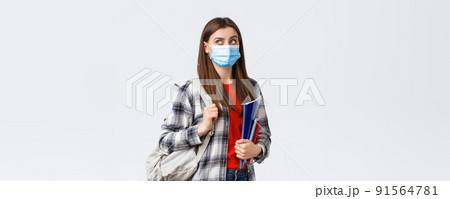Coronavirus pandemic, covid-19 education, and back to school concept. Smart female student, freshman girl heading to class, look upper left corner interested at banner, hold notebooks and backpack 91564781