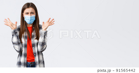 Different emotions, covid-19 pandemic, coronavirus self-quarantine and social distancing concept. Angry, outraged woman in medical mask, arguing, look mad, raise hands in dismay, complaining 91565442