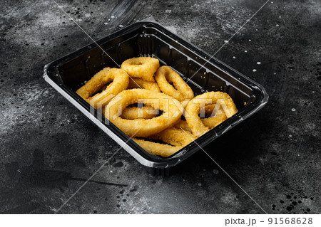 Frozen raw squid or onion rings breaded, on black dark stone table background 91568628