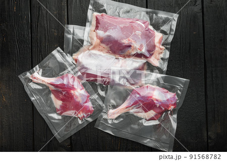 Fresh uncooked duck meat, legs and breast vacuum sealed, on black wooden table background, top view flat lay Fresh uncooked duck meat, legs and breast vacuum sealed, on black wooden table background, top view flat lay 91568782