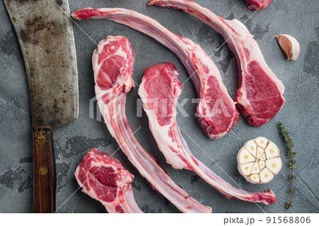 Raw fresh lamb loin chops, with ingredients carrot orange, herbs, and old butcher cleaver knife, on gray stone background, top view flat lay Raw fresh lamb loin chops, with ingredients carrot orange, herbs, and old butcher cleaver knife, on gray stone background, top view flat lay 91568806