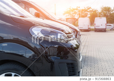 Close-up detail headlight view of many modern luxury black vans parked in row at car sale rental leasing dealer against sunset. Commericial trasfer cargo transportation company fleet. Vip charter Close-up detail headlight view of many modern luxury black vans parked in row at car sale rental leasing dealer against sunset. Commericial trasfer cargo transportation company fleet. Vip charter 91568863