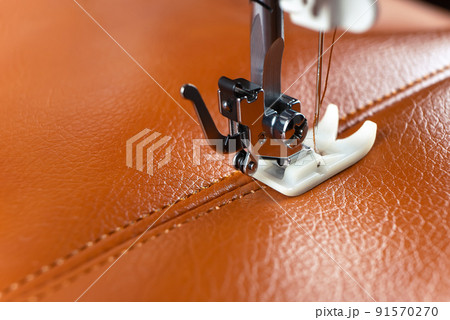 Modern sewing machine presser foot with a needle sews brown leather 91570270