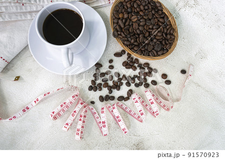 Cup of coffee and coffee beans background with measure tap on white desk. Cup of coffee and coffee beans background with measure tap on white desk. 91570923