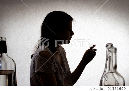 Woman holds a glass with strong alcohol. Female alcoholism, alcohol addiction, delirium tremens. Silhouette photo. Woman holds a glass with strong alcohol. Female alcoholism, alcohol addiction, delirium tremens. Silhouette photo. 91571699