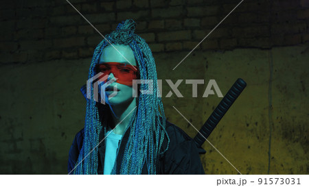 girl with dreadlocks and katanas in red glasses posing against a neon brick wall girl with dreadlocks and katanas in red glasses posing against a neon brick wall 91573031