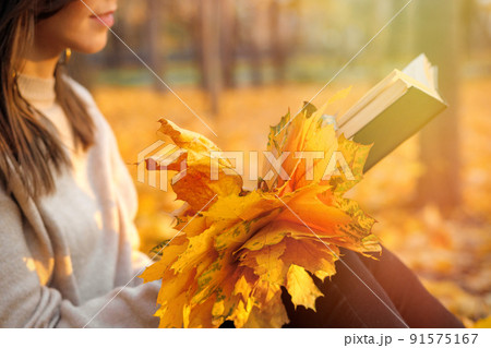 Close-up on an autumn bouquet of yellow leaves and a book on a woman's lap. Enjoying the last warm autumn days Close-up on an autumn bouquet of yellow leaves and a book on a woman's lap. Enjoying the last warm autumn days 91575167