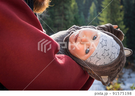 Portrait of little baby traveler in a funny jumpsuit with ears in the arms of a parent 91575198