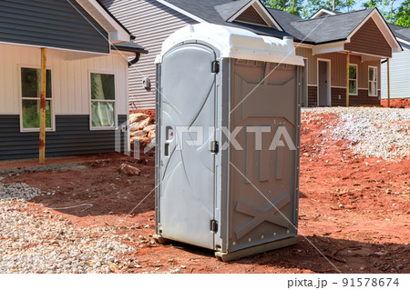 A portable restroom is being used at a construction site near a house that is being built 91578674