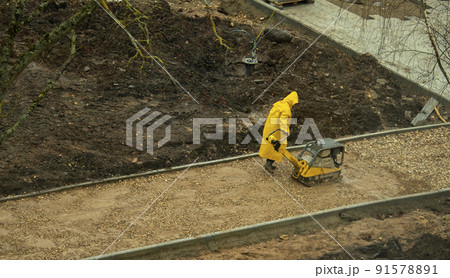 a worker in a yellow raincoat rams the sand before laying asphalt a worker in a yellow raincoat rams the sand before laying asphalt 91578891