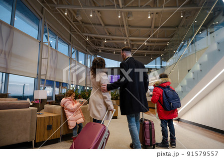 Traveling family with suitcases checking flight information on board with timetable, standing in airport departures terminal, waiting to board flight 91579557
