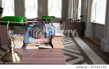 Senior man falls asleep over a textbook, he is sitting at a table 91581149