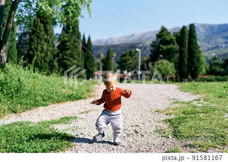 Kid walks along the path among the trees against the background of mountains Kid walks along the path among the trees against the background of mountains 91581167