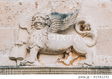 A bas-relief on the wall depicting a mythical lion with wings and a book in its paws. A bas-relief on the wall depicting a mythical lion with wings and a book in its paws. 91581242