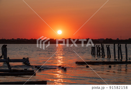 Beautiful red and orange sunset over the sea. The sun goes down over the sea. A flock of cormorants sits on a old sea pier in orange sunset light Beautiful red and orange sunset over the sea. The sun goes down over the sea. A flock of cormorants sits on a old sea pier in orange sunset light 91582158