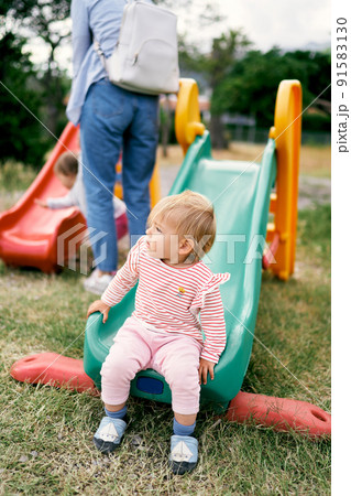 Kid sits on a children's slide on a playground in a green park 91583130