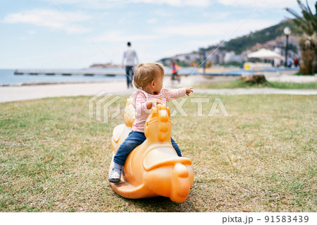Little kid sitting on a swing in the playground on the beach Little kid sitting on a swing in the playground on the beach 91583439