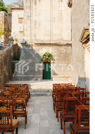 Wooden chairs with patterns on the backs stand in rows on the cobblestones in front of the church door 91583825