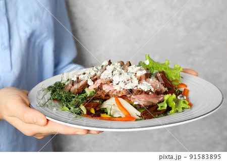 Woman holding plate with delicious salad on grey background, closeup 91583895