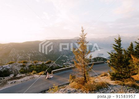Bride and groom are walking along the road in the mountains against the backdrop of the bay. Drone Bride and groom are walking along the road in the mountains against the backdrop of the bay. Drone 91583957