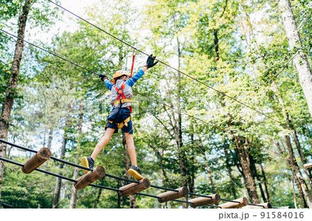 Boy walking on the agility bridge holding on to the ropes Boy walking on the agility bridge holding on to the ropes 91584016