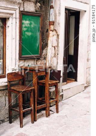 Wooden high table and two chairs near the wall of a small bar on the street Wooden high table and two chairs near the wall of a small bar on the street 91584175