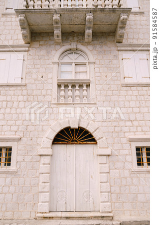 Facade of a building with an arched door, shutters on the windows and a stone balcony Facade of a building with an arched door, shutters on the windows and a stone balcony 91584587