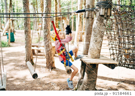 Boy in a safety belt climbs onto a tree platform across the agility bridge 91584661