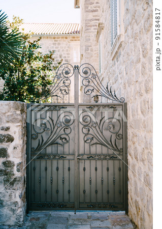 Forged openwork gate near the wall of a stone house with shutters 91584817