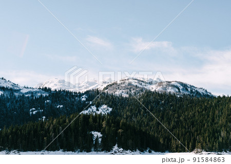 Black lake against the background of a green coniferous forest and snow-capped mountains. Montenegro 91584863