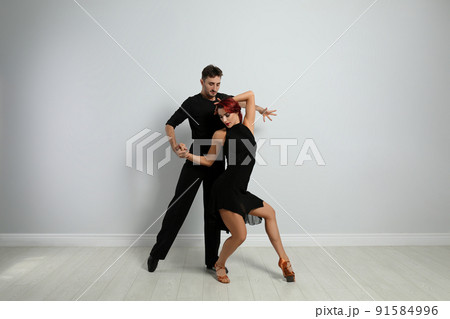 Beautiful young couple dancing near light wall Beautiful young couple dancing near light wall 91584996