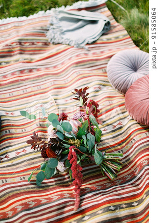 Wedding bouquet lies on a colorful bedspread next to round pillows and a blanket Wedding bouquet lies on a colorful bedspread next to round pillows and a blanket 91585064