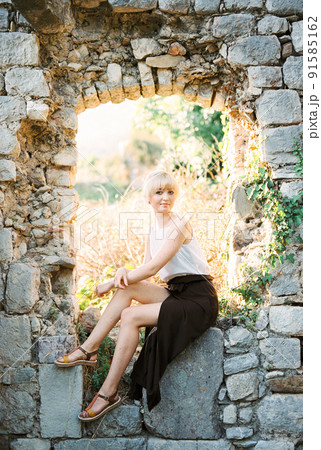 Woman sits on a window in the stone ruins of an old fortress 91585162