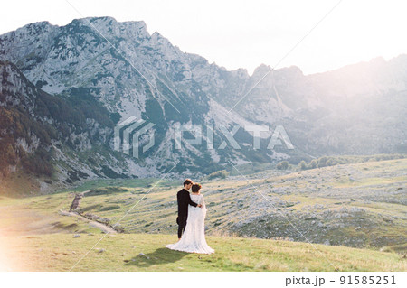Bride and groom stand in the valley and look at the mountains. Back view Bride and groom stand in the valley and look at the mountains. Back view 91585251