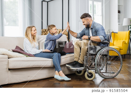 Child making high five gesture with disabled father at home Child making high five gesture with disabled father at home 91585504