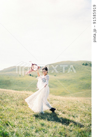 Girl in a white dress walks through a green valley, raising a tambourine above her head Girl in a white dress walks through a green valley, raising a tambourine above her head 91585919
