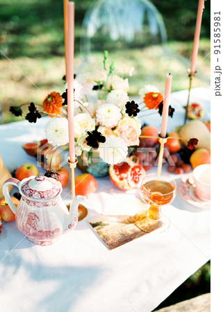 Bouquet of flowers next to fruits and candles stands on a table in the garden Bouquet of flowers next to fruits and candles stands on a table in the garden 91585981