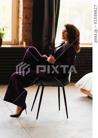 a young brunette woman in a purple pantsuit on the background of the window  91586627
