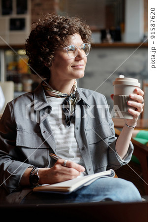 Young pensive businesswoman or freelancer with pen over page of copybook 91587620