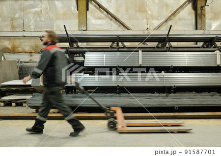 Side view of blurry outline of male engineer passing by stack od metallic planks 91587701