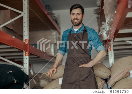 Warehouse worker standing near bags with coffee beans in the coffee small factory Warehouse worker standing near bags with coffee beans in the coffee small factory 91591750