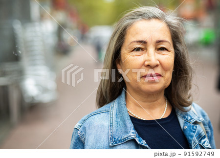 Portrait of positive elderly woman walking along city street 91592749