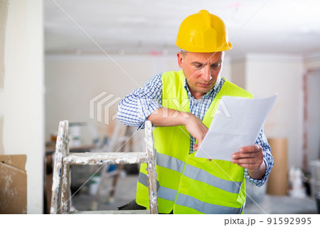 Man with documents in her hands stands in the middle of renovated room in cottage 91592995
