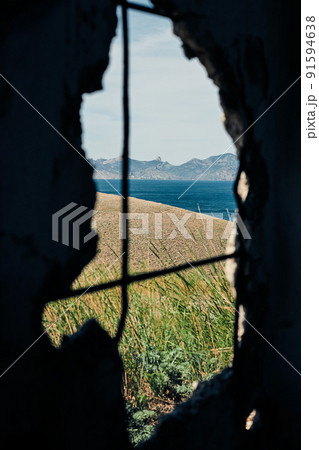 The sea and the rocks on the south coast. Crimea, landscape on a sunny day. View through a hole in the wall. Vertical photo. The sea and the rocks on the south coast. Crimea, landscape on a sunny day. View through a hole in the wall. Vertical photo. 91594638