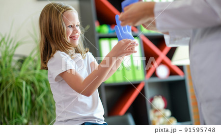 Doctor and little girl having fun disposable gloves in clinic 91595748