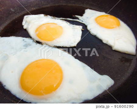 3 fried eggs frying in a pan with olive oil. Three fried eggs in cast iron frying pan sprinkled with ground black. 91600290